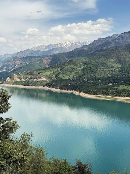A calm lake surrounded by green hills and snow-capped mountains under a clear sky. 3
