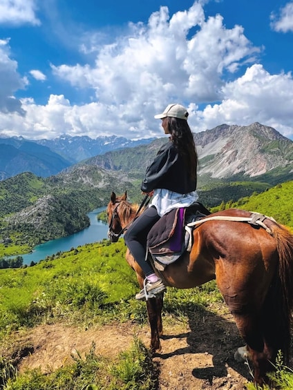 A person riding a horse across a mountainous landscape with a lake and distant mountains. 1