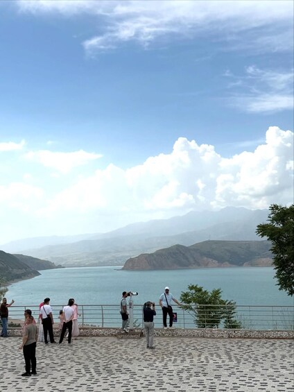A group of people taking photos of a lake with mountains in the background. 2