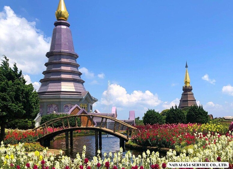 A pagoda with a golden spire, a bridge over a pond, and a garden with colorful flowers. 1