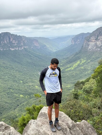 A person standing on a rock with a mountainous landscape in the background. 4