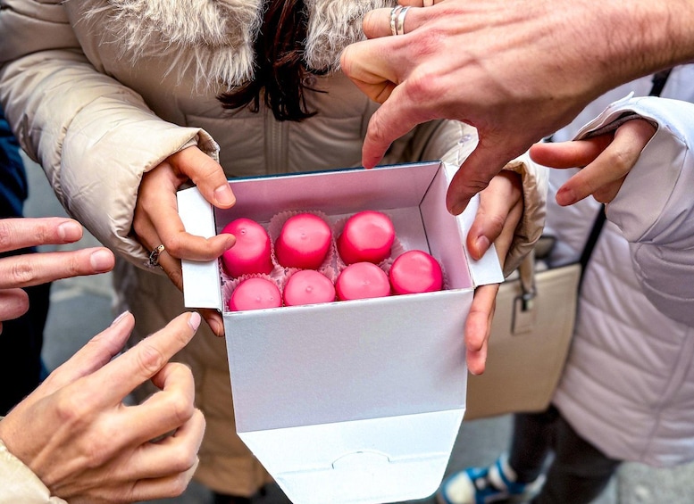A person holding a box of pink round objects. 3