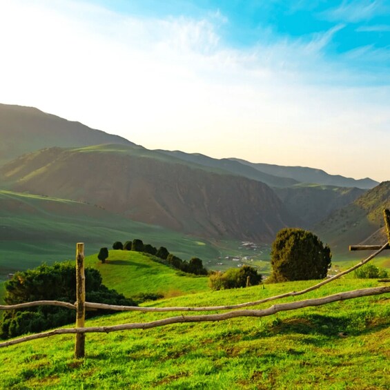 Rolling green hills, a wooden fence, and distant mountains under a clear sky. 1