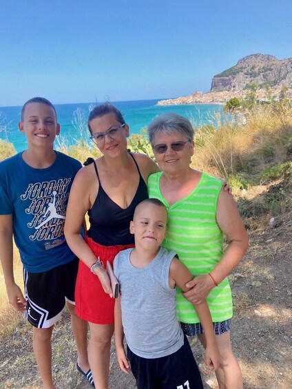En familj på fyra personer står på en kuststig med utsikt över havet och en bergig kulle i bakgrunden. 2