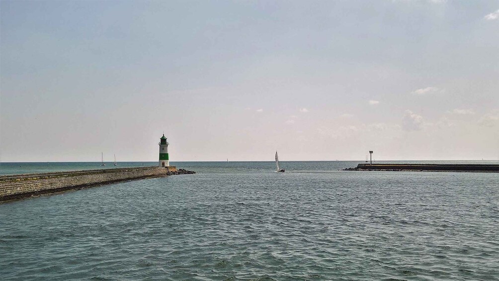 A lighthouse, a pier, and a sailboat on calm waters. 3