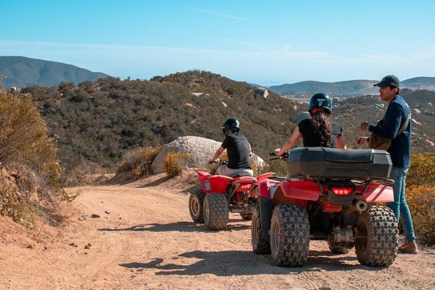 A dirt road with off-road vehicles, rocky terrain, and hills in the background. 3
