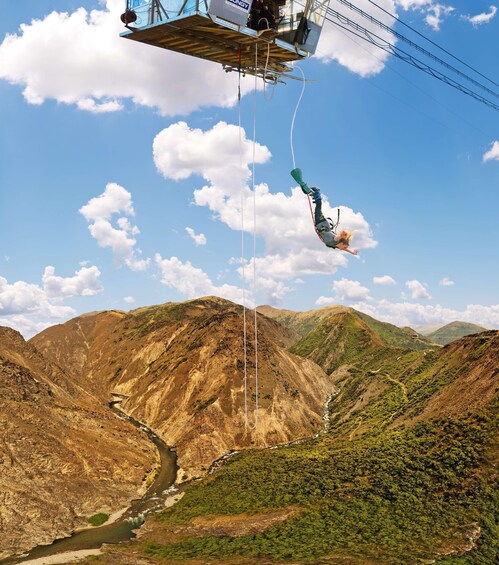 A person bungee jumping from a bridge over a canyon with a river below and mountains in the background. 4