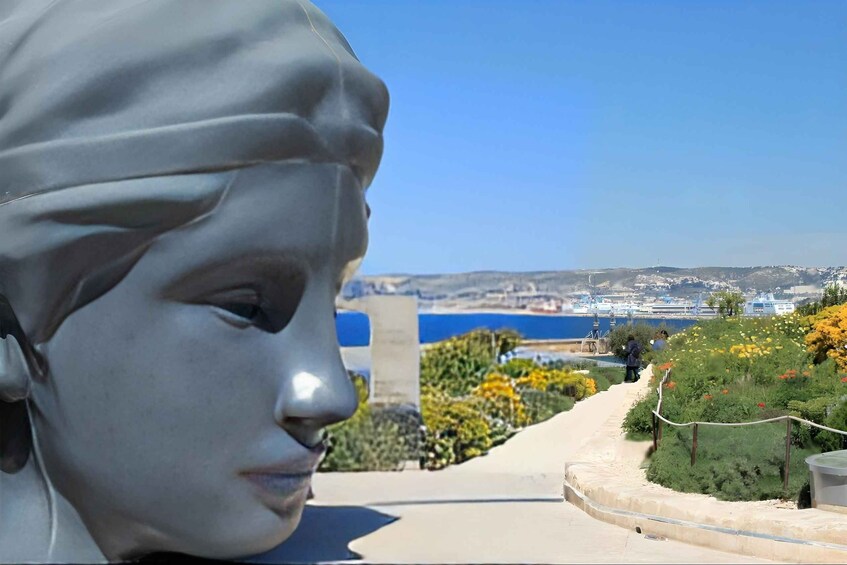 A statue, a pathway, and a coastal landscape with buildings in the distance. 2