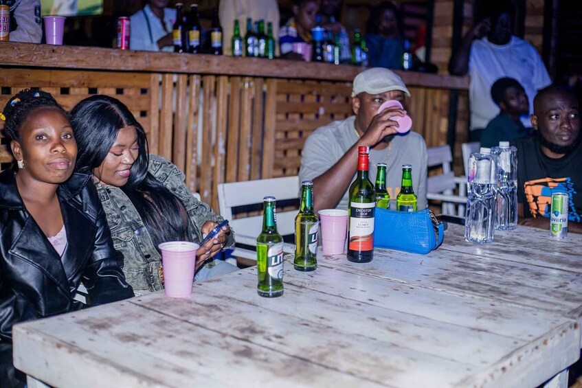 A group of people at a bar with bottles and cups on the table. 1