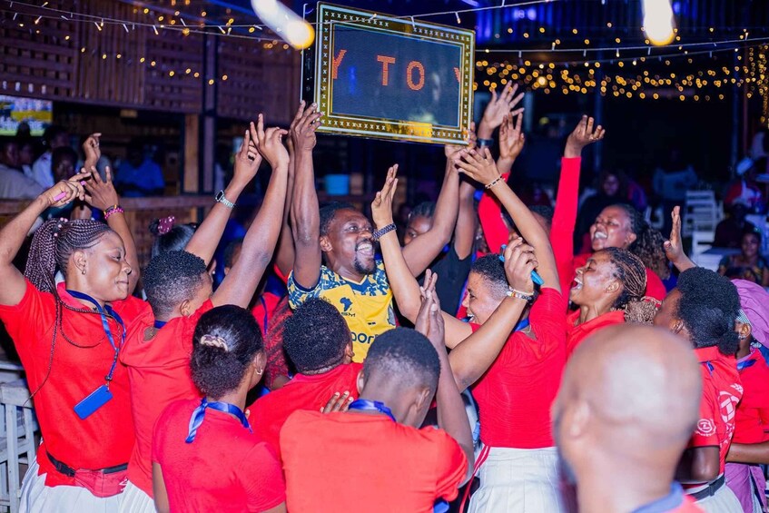 A group of people in red shirts celebrating with a sign that reads "TO". 3