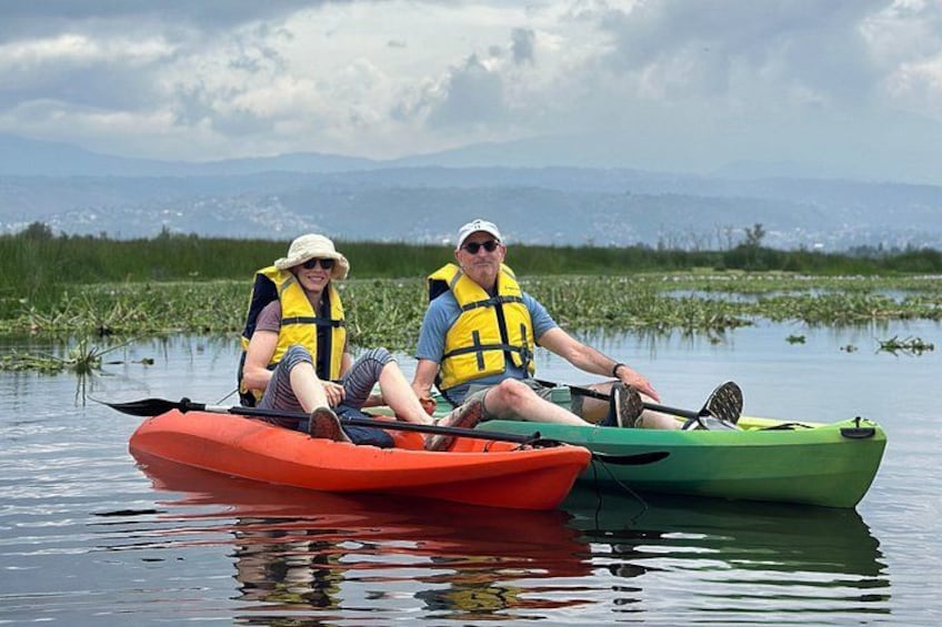 Dos personas remando en kayak sobre aguas tranquilas, con un paisaje montañoso al fondo. 5