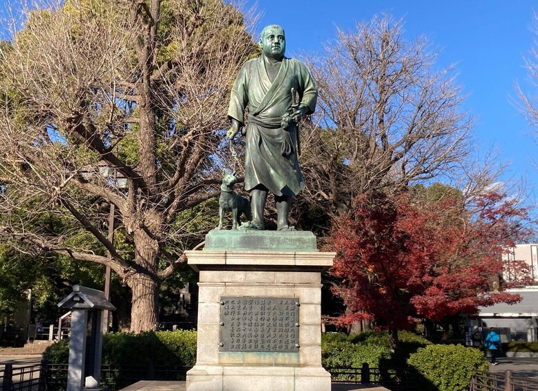 A statue of a man in traditional attire with a dog, surrounded by trees and a stone plaque. 5