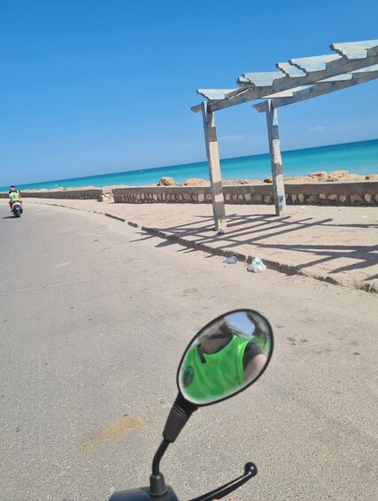 A motorcycle on a paved road with a beach and a wooden structure in the background. 2