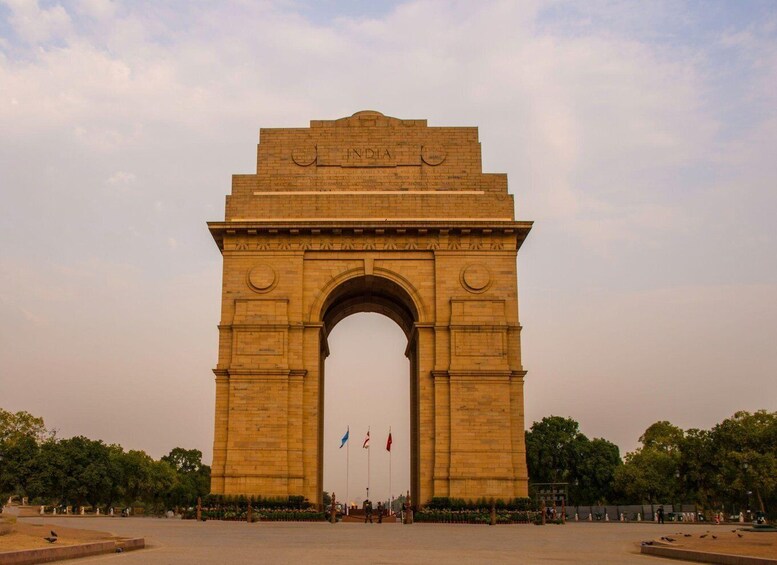 A large stone archway with inscriptions, surrounded by a spacious plaza with trees and a few people. 3