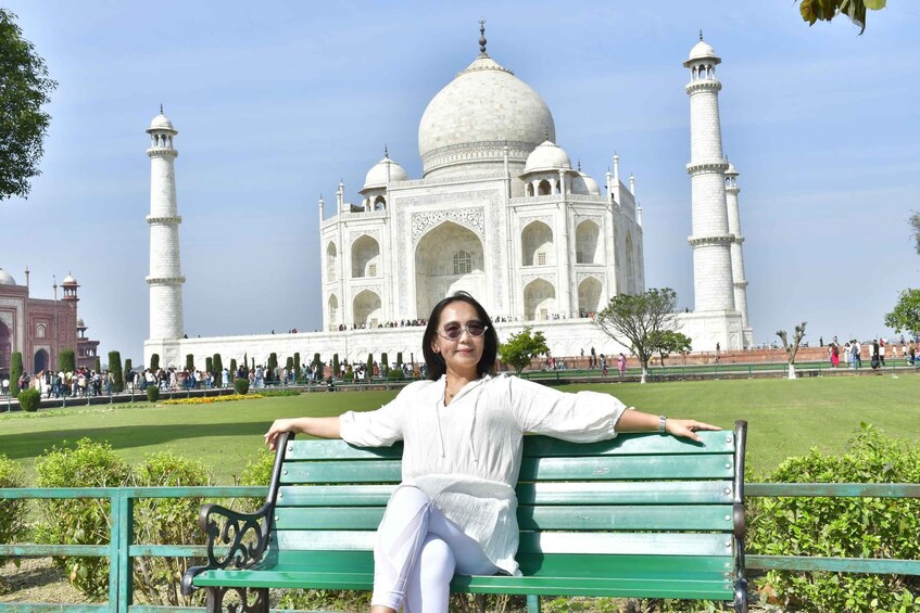 A person sitting on a green bench with the Taj Mahal in the background. 5