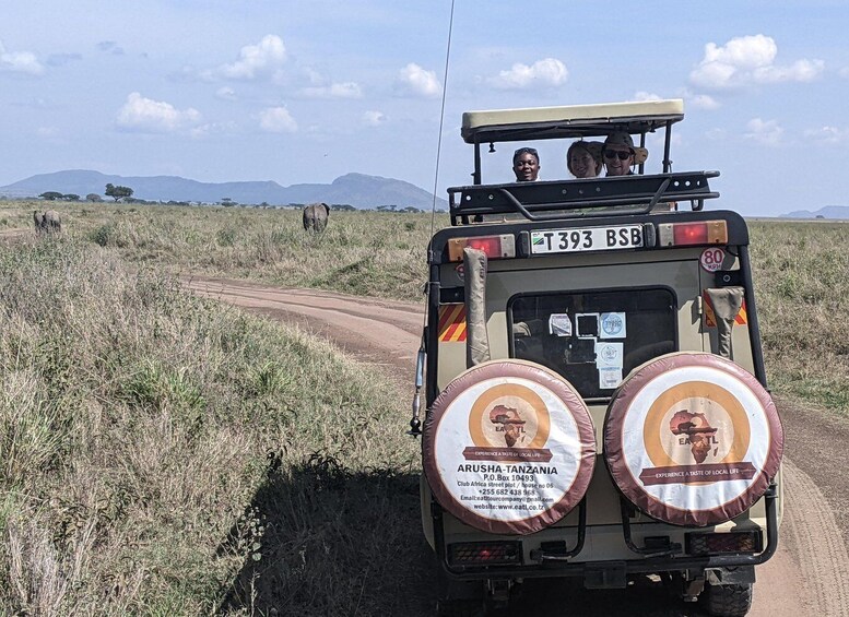 Un veicolo safari con due grandi cartelli circolari sul retro, una targa e un cielo sereno con montagne in lontananza. 3