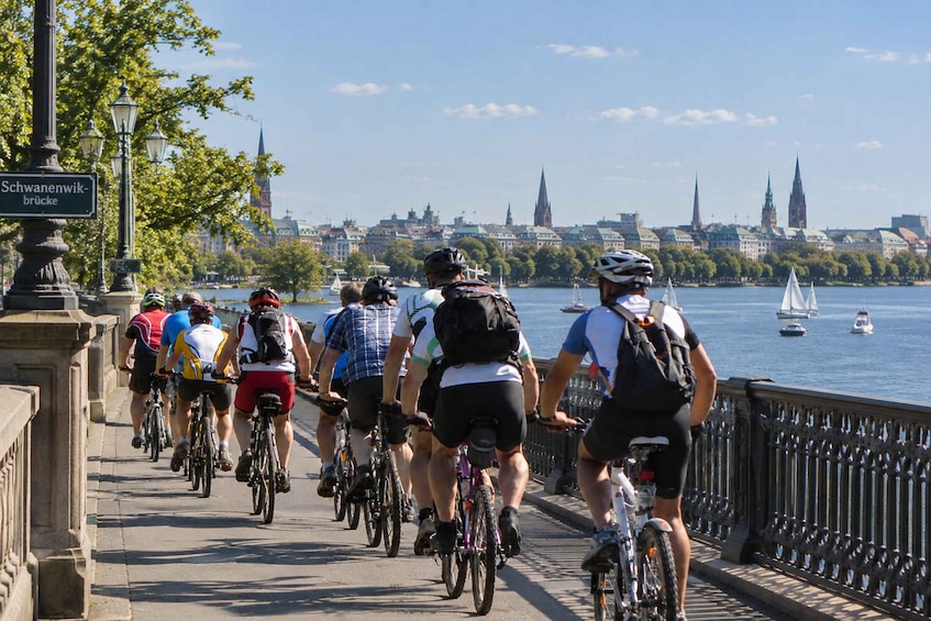 A group of cyclists on a bridge with a cityscape and river in the background. 1