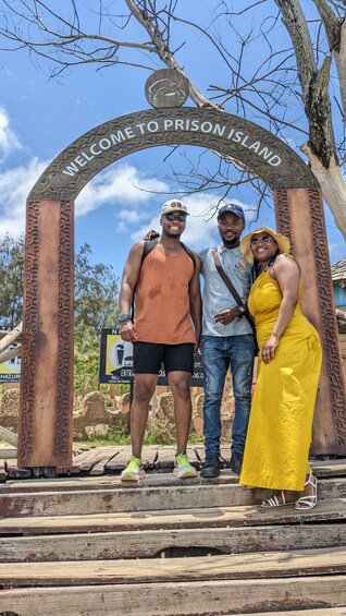 A sign reading "Welcome to Prison Island" with three people standing in front. 5