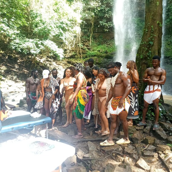 A group of people standing near a waterfall in a forested area. 5