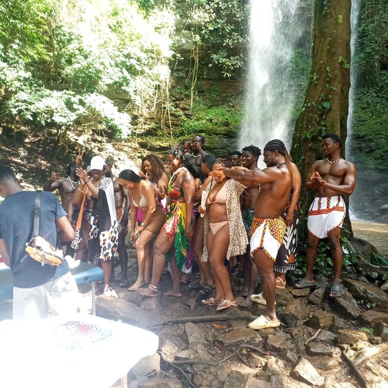 A group of people standing by a waterfall in a forested area. 3