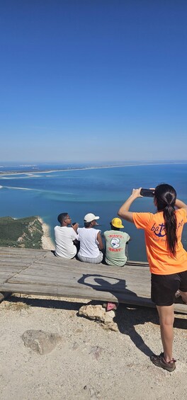 Four people sitting on a wooden platform overlooking a beach and ocean. 5