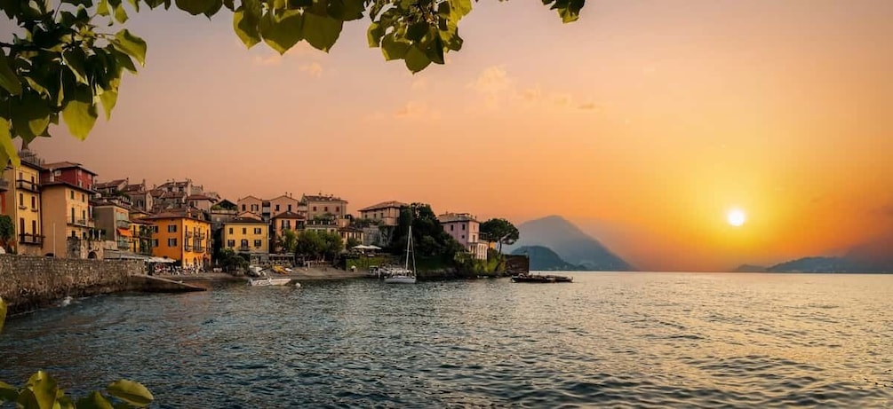 A coastal town with buildings along the water, a sunset, and a mountain in the background. 5