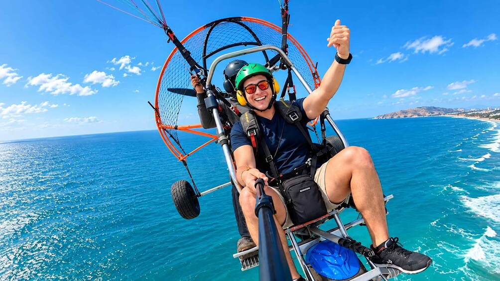 A person in a paragliding harness with a clear view of the ocean and coastline. 5
