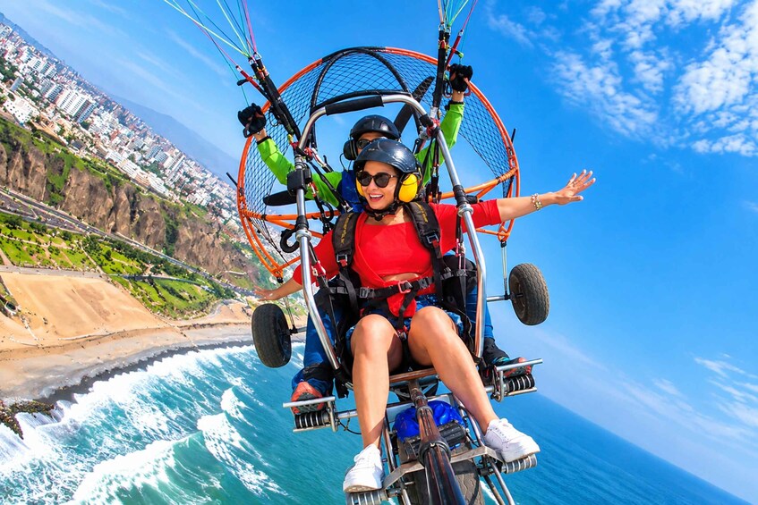 A person on a paragliding harness with a cityscape and coastline in the background. 3