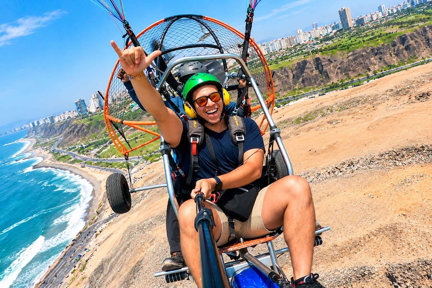 A person in a harness and helmet, seated in a wing chair, overlooking a coastal city with a beach and cliffs. 4