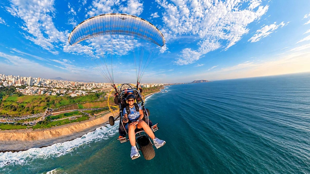 A person paragliding over a coastal city with a clear sky and ocean below. 1