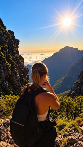 A person sitting on a rocky outcrop with a backpack, overlooking a mountainous landscape with a sun shining in the background. 2