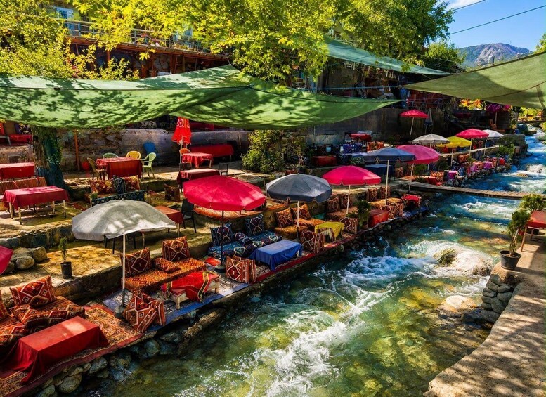 A riverside restaurant with outdoor seating, umbrellas, and a flowing river. 1