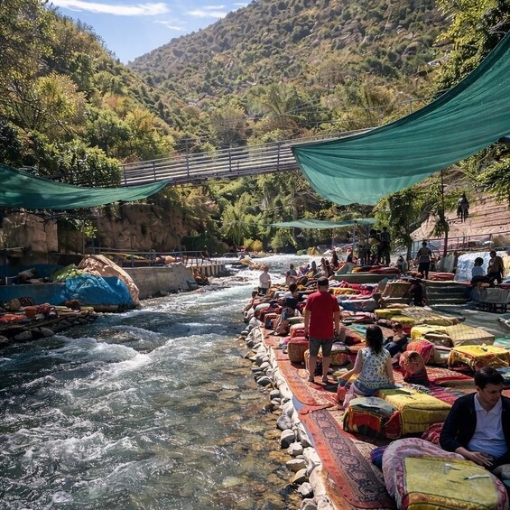 A river with people sitting on mats and a bridge in the background. 2