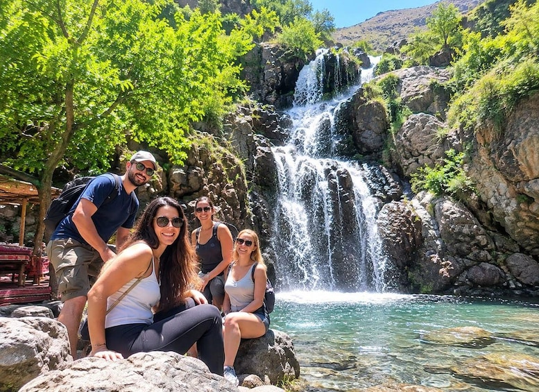 A group of people sitting on rocks by a waterfall in a natural setting. 2