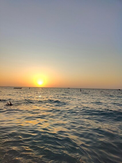 Tramonto su un mare calmo, con barche e una costa in lontananza. 3