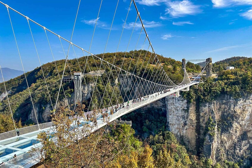 A suspension bridge with people walking across it, surrounded by forested hills. 3