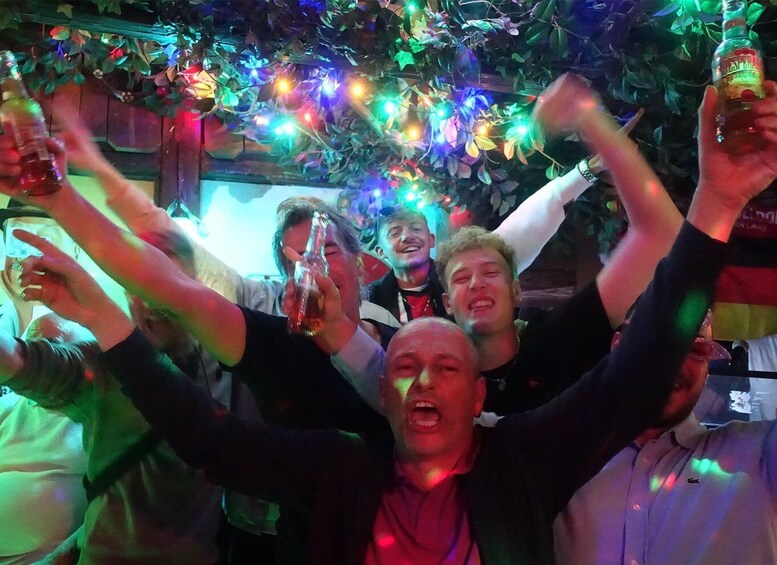 A group of people celebrating with drinks, surrounded by colorful lights and greenery. 4