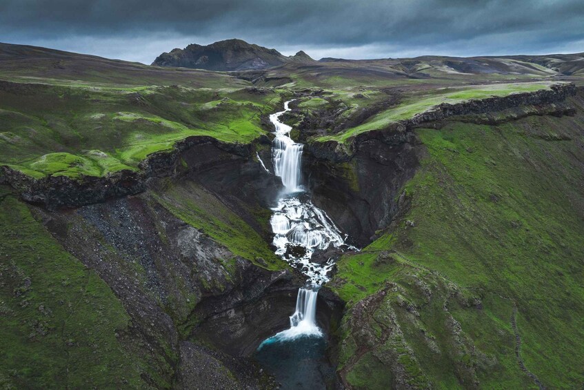 A waterfall cascading down a rocky gorge surrounded by green hills. 3
