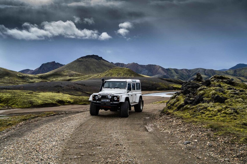 A white Land Rover driving on a gravel road surrounded by mountains and grassy terrain. 2