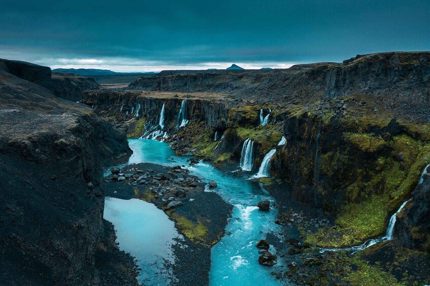 A river with multiple waterfalls surrounded by rugged terrain and sparse vegetation. 1