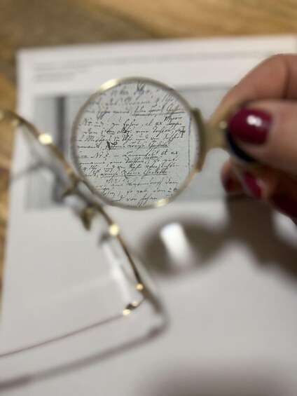 A hand holding a magnifying glass over a document with handwritten text. 1
