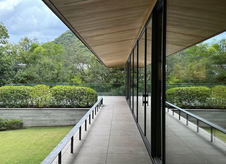 A covered walkway with glass railings, surrounded by neatly trimmed hedges and trees. 1