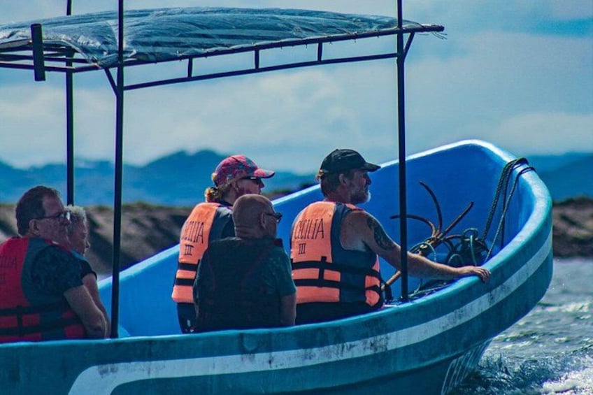 A group of people on a blue boat with life jackets, a person steering, and a mountainous landscape in the background. 2