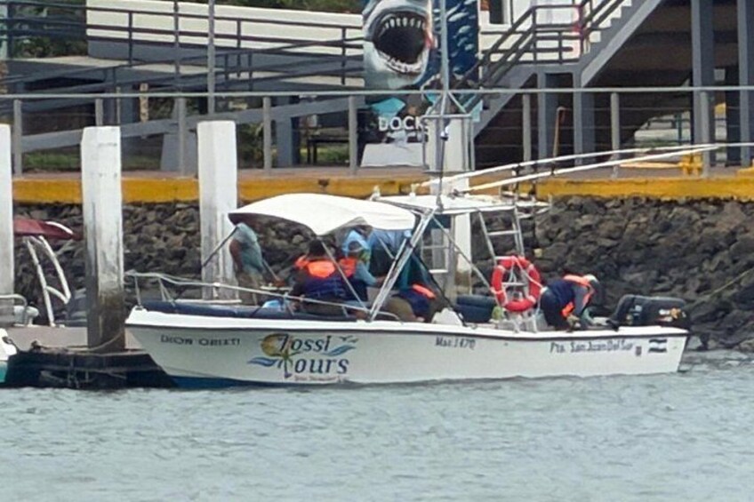 A boat named 'Dossil Tours' docked at a pier with a lifebuoy and a person wearing a life jacket. 4