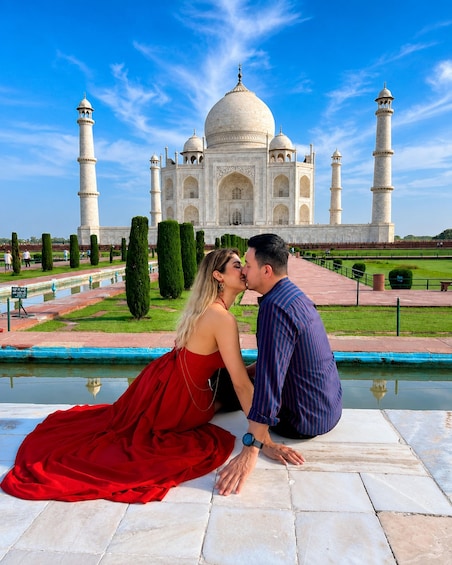 Pariskunta suutelee Taj Mahalin edessä, taustalla kirkkaan sininen taivas. 1