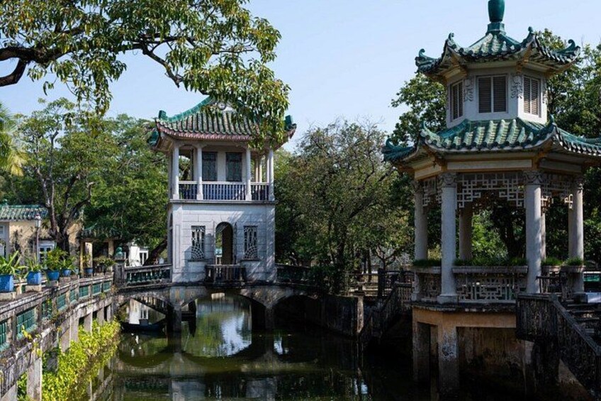 A traditional Chinese pavilion with a tiled roof, a small bridge over a water body, and lush greenery in the background. 5