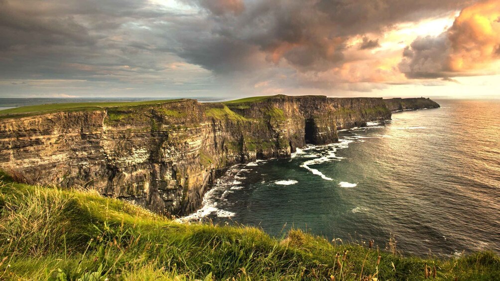 A coastal cliff with waves crashing against it, under a cloudy sky. 2