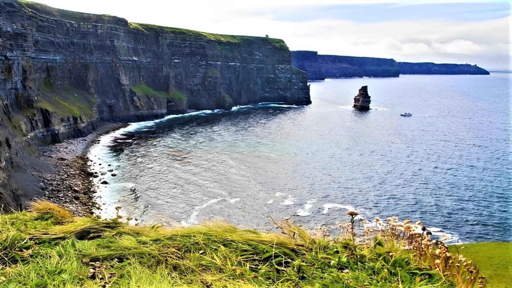 A coastal cliff with a rocky shoreline and a prominent rock formation in the sea. 1