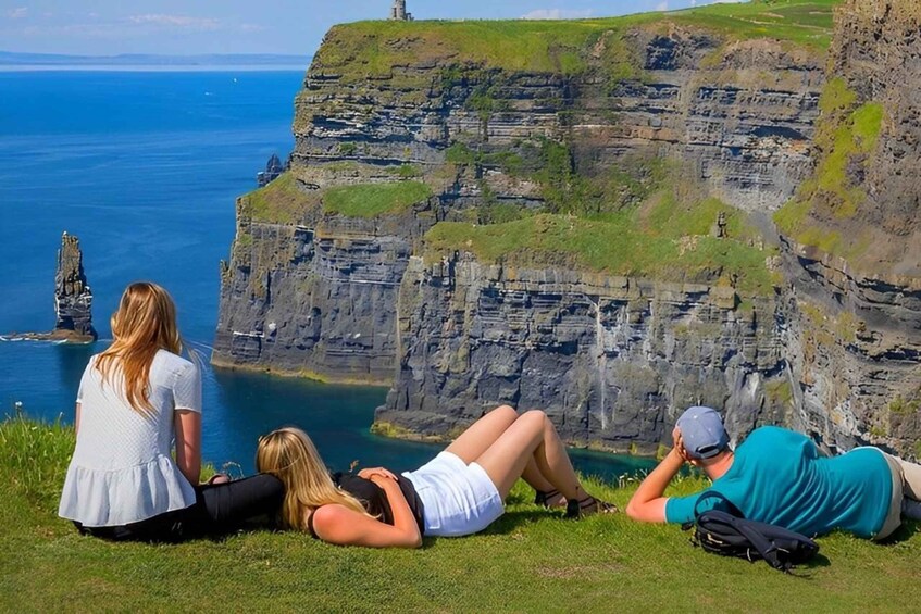 A group of people sitting on a grassy cliff overlooking a deep blue sea and a rocky coastline. 3