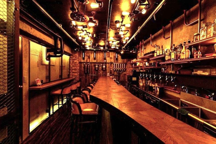 A bar with wooden bar stools, a long counter, and shelves stocked with bottles. 2